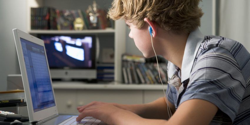 Young boy in bedroom using laptop and listening to MP3 player the Real Cost of Raising Kids
